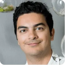 Portrait of a smiling young man with dark curly hair and light skin wearing a white shirt.